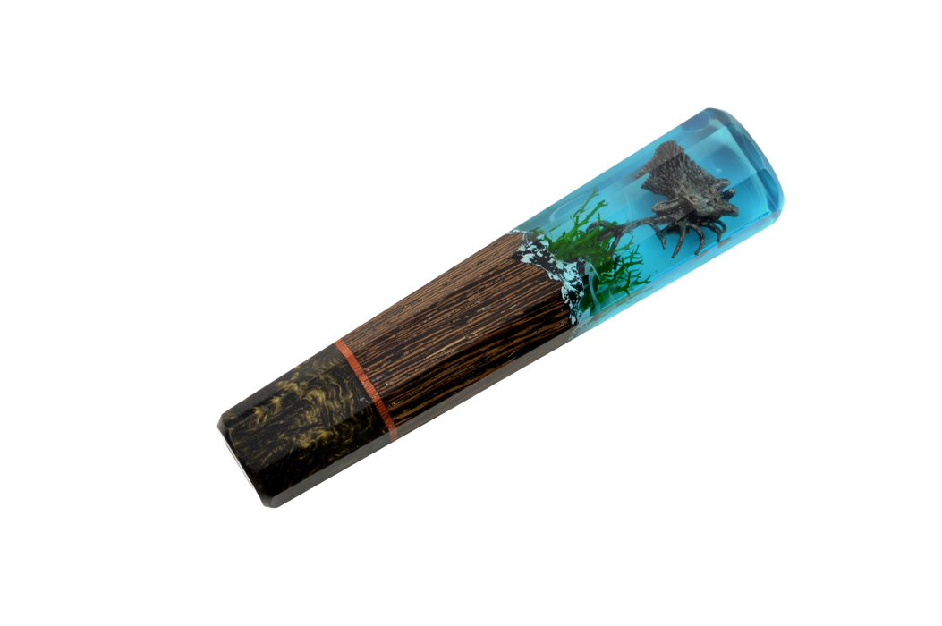 The Custom Wa-Handle #634 - 137mm (Standard) by Made in Turkey features a textured brown log, green moss, and a detailed black spider encased in clear blue resin, echoing the natural elegance of custom knife handles.