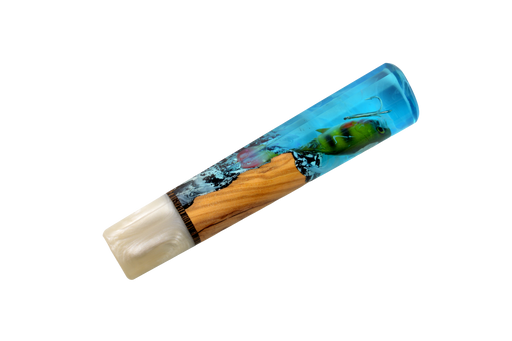 Le modèle « Made in Turkey Custom Wa-Handle #629 » (142 mm, standard) se compose d'une partie en résine bleue évoquant l'eau, ornée d'un leurre de pêche vert, d'un segment en bois rappelant le manche d'un couteau sur mesure, et d'une extrémité blanc nacré, le tout présenté sur fond blanc.